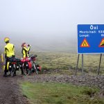 Dimma med två cyklister vid vägskylt om brant nerförsbacke.